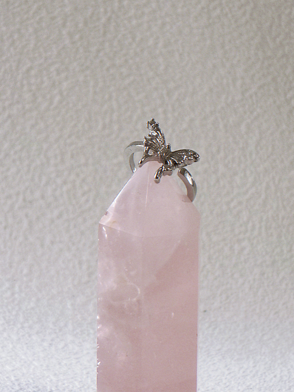 Silver ring with a small butterfly design on a pink crystal against a light gray background