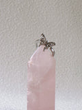 Silver ring with a small butterfly design on a pink crystal against a light gray background