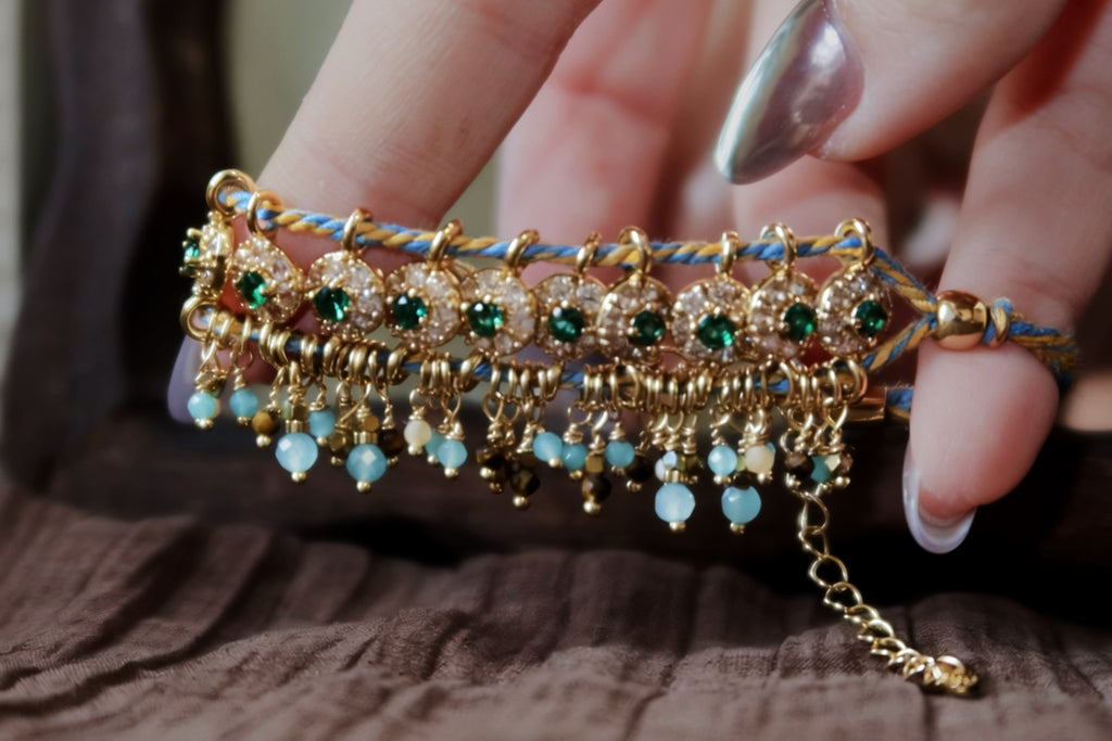 Close-up detail of the Peacock's Muse antique green hand-woven bracelet, focusing on the meticulous handcrafted braided cords, glowing green glass beads, and natural tiger's eye chatoyancy.