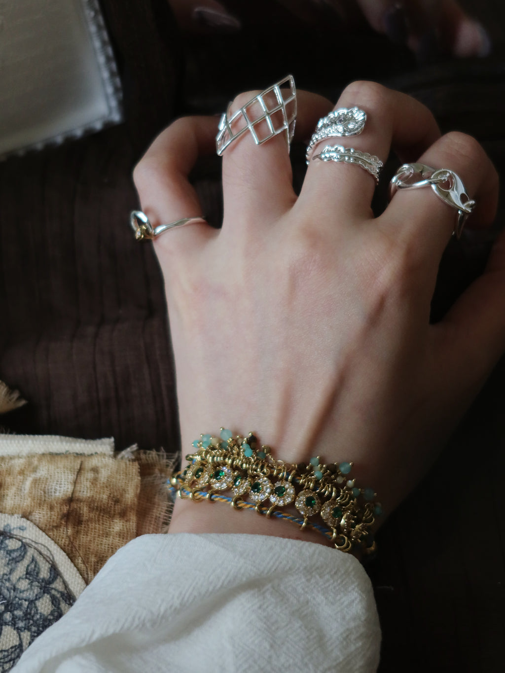 A model's hand styling The Peacock’s Muse antique green hand-woven bracelet stacked with multiple silver statement rings, featuring a romantic French vintage aesthetic.