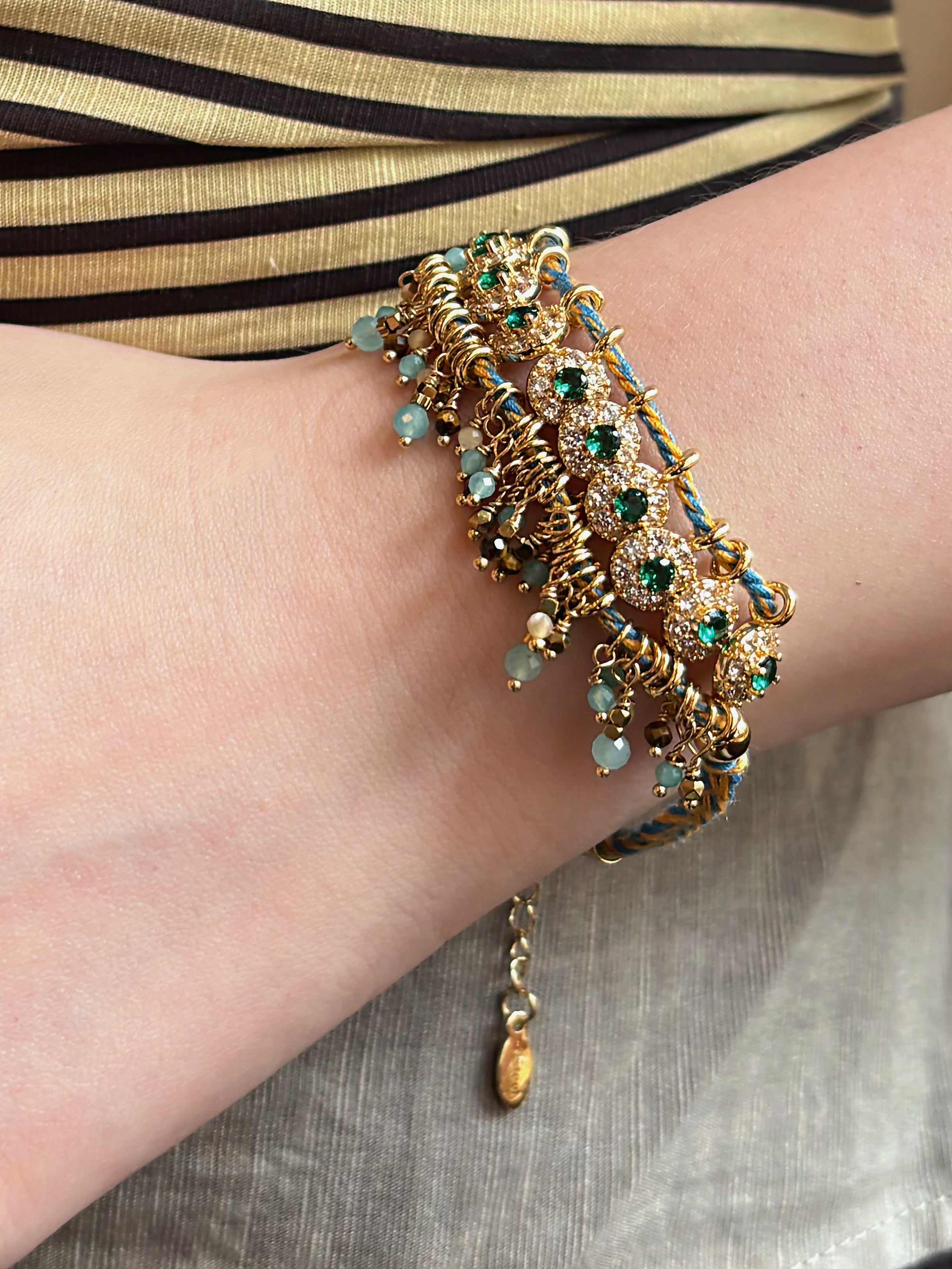 A close-up picture of a model wearing hand-woven green and yellow bohemian free feeling bracelet, showcasing a structured row of green glass beads, natural tiger's eye, and micro-paved green zircons