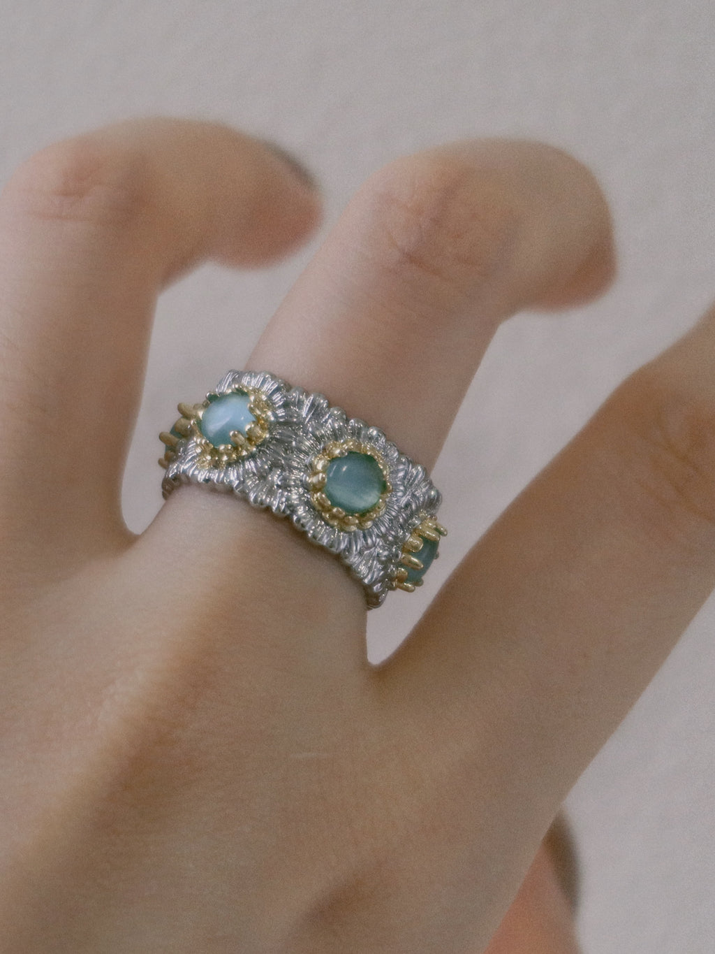 Close-up of a hand wearing an ornate ring with green gemstones on a neutral background