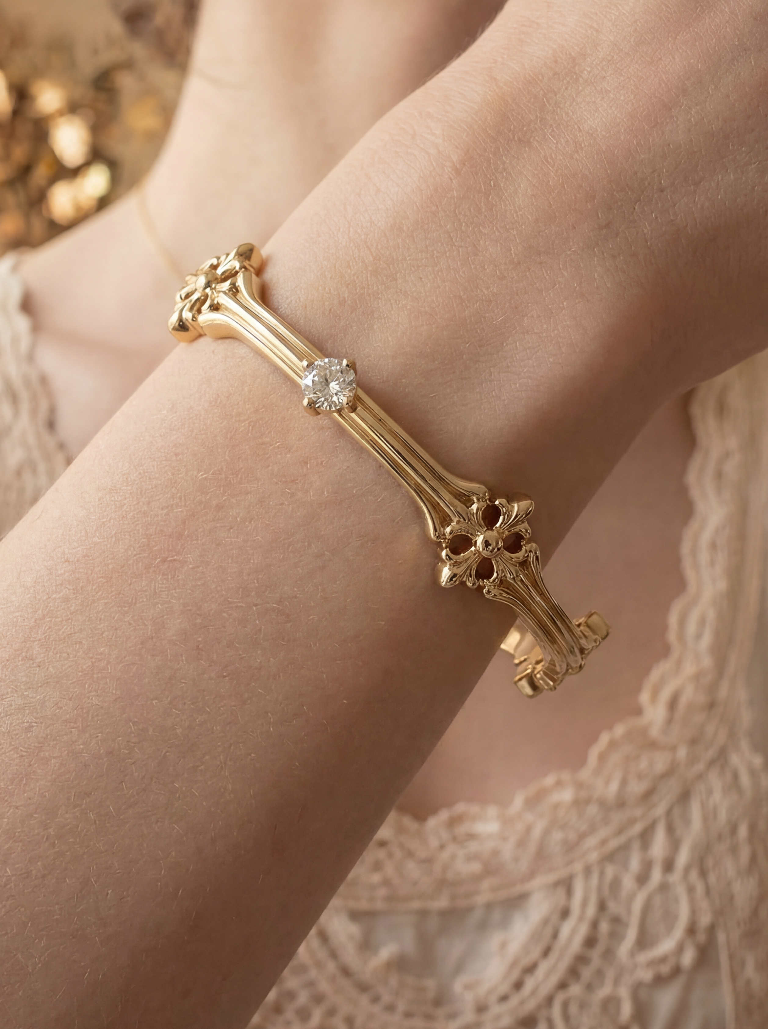 Gold bracelet with a diamond on a person's wrist, wearing a lace dress.