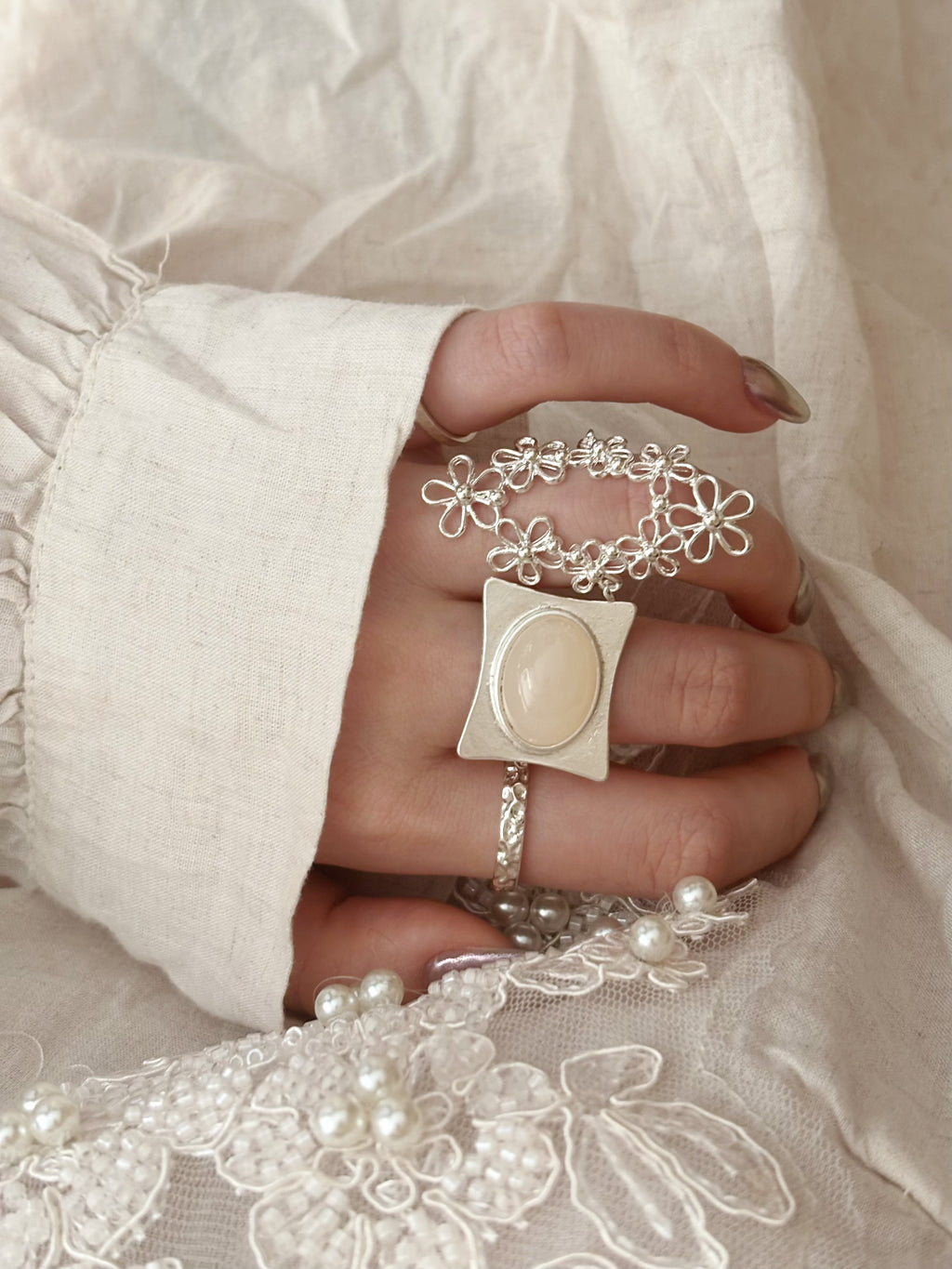 An on-model view of the French vintage oval filigree lace ring stacked with a statement gemstone ring, perfectly complemented by a beaded embroidered linen garment.