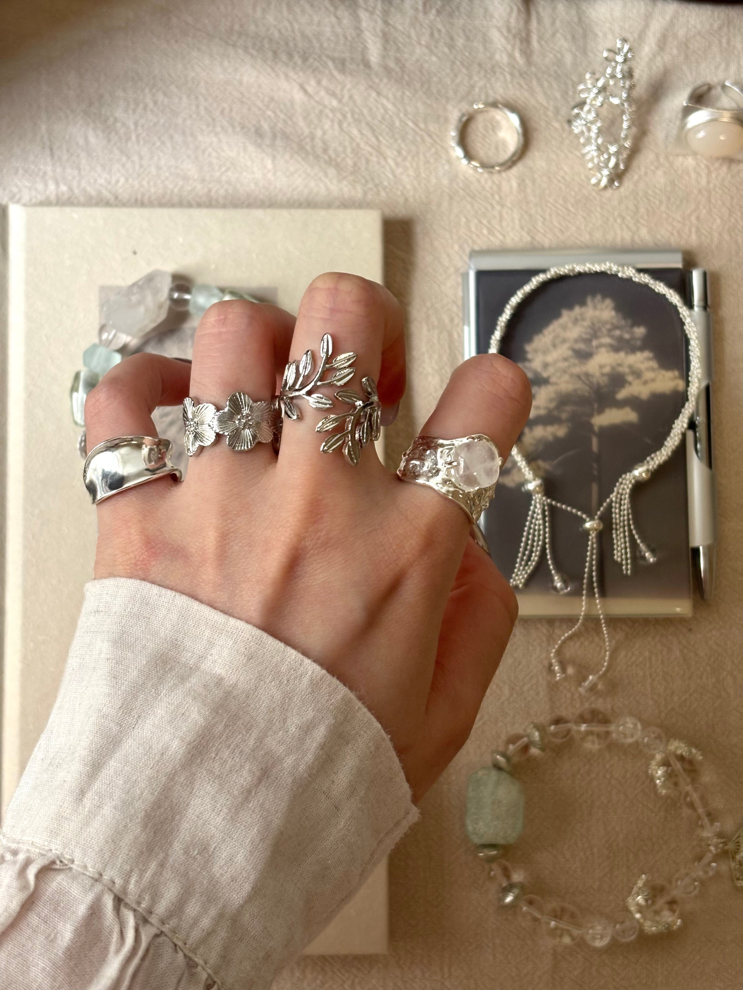 A hand wearing multiple silver rings with floral and leaf motifs. Wild rose ring among vintage silver jewelry pieces.
